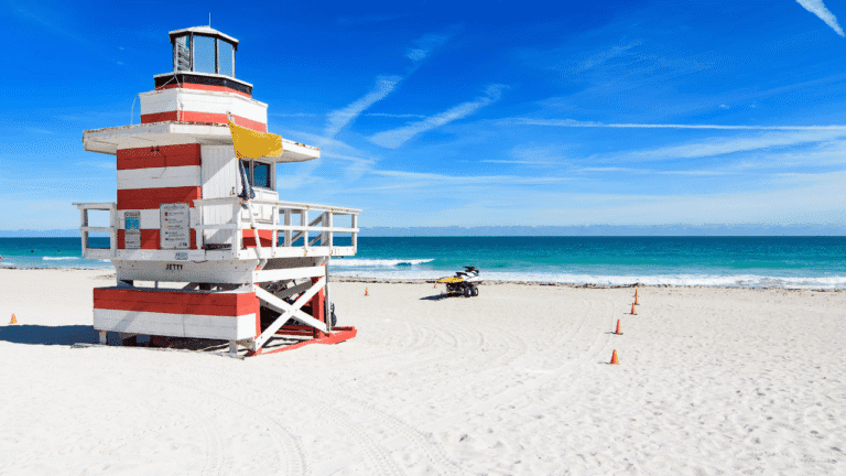 Primo piano della spiaggia di sabbia chiara di Miami Beach con le tipiche passerelle in legno, bagnanti in lontananza e le onde calme dell'oceano che si infrangono sulla riva.