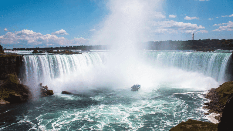 Fotografia panoramica che mostra lo skyline moderno di Toronto riflesso sul lago e il maestoso salto d'acqua delle Cascate del Niagara con l'arcobaleno che si forma tra i vapori.