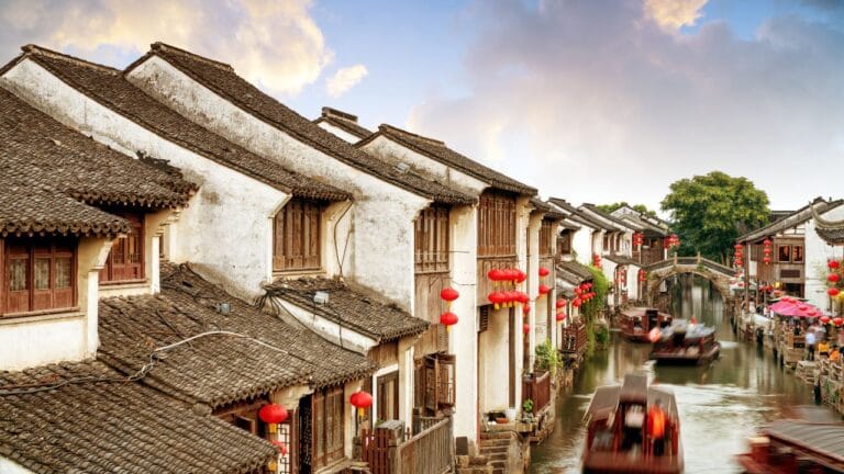 Scorcio suggestivo di Suzhou, Cina: case tradizionali lungo i canali, lanterne rosse e imbarcazioni tipiche in un viaggio di gruppo organizzato.