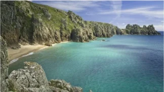 Vista dall'alto della spiaggia di Pedn Vounder in Cornovaglia, Regno Unito, con scogliere di granito lussureggianti e acqua turchese cristallina.