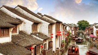 Scorcio suggestivo di Suzhou, Cina: case tradizionali lungo i canali, lanterne rosse e imbarcazioni tipiche in un viaggio di gruppo organizzato.
